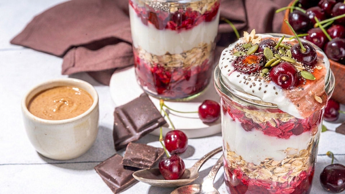 Chocolate cherry overnight oats in a glass jar topped with cherries, pumpkin seeds, and chia seeds, with almond butter and dark chocolate on the side