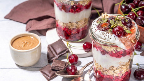 Chocolate cherry overnight oats in a glass jar topped with cherries, pumpkin seeds, and chia seeds, with almond butter and dark chocolate on the side