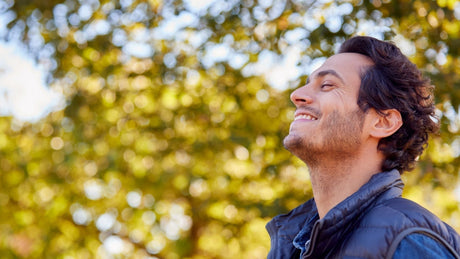 Man relaxing outdoors in an autumn park, breathing deeply among fall trees during a seasonal wellness reset